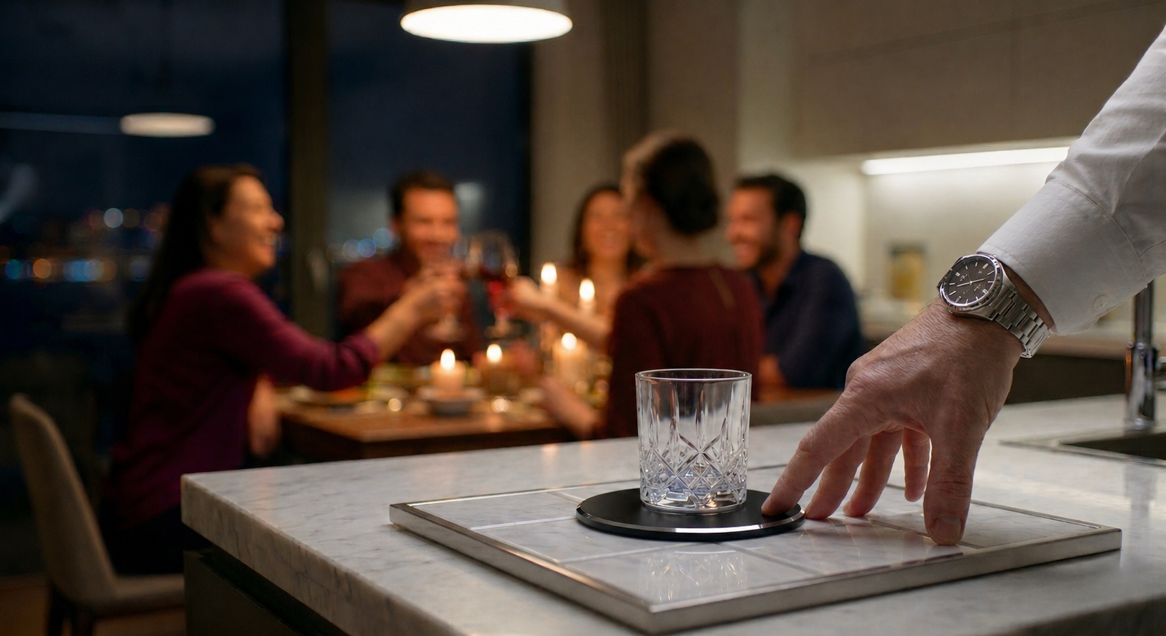 A detailed close-up photograph of a man's right hand wearing a white cuff and a silver-link watch. His index finger is making contact with the base of a crystal-patterned whiskey tumbler filled with water. The tumbler is resting centered on a circular, black, stitched-edge leather coaster. This coaster is placed upon a white marble serving tray with distinct grid lines, resting on a white marble countertop. In the blurred bokeh background, a candlelit dinner table with four people laughing and raising wine glasses is visible through a large window overlooking the Istanbul Bosphorus and bridge at night. The man is completely disconnected from the social gathering.